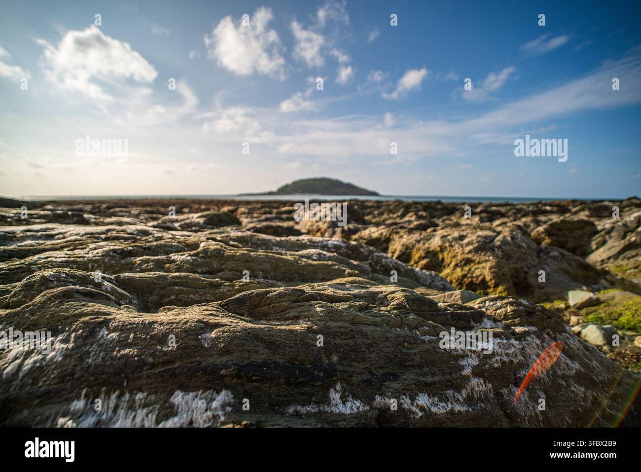 Arrière-plan rocheux de Hannafore Beach avec Looe Island visible à l'horizon sous un ciel bleu parsemé de nuages. Banque D'Images