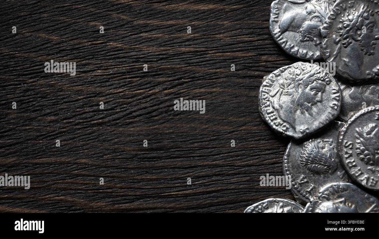 Une photographie en vue plongeante, en flat lay, mettant en scène un groupe de pièces d'argent anciennes reposant sur une surface en bois rustique sombre et fortement texturée. Les pièces, posi Banque D'Images