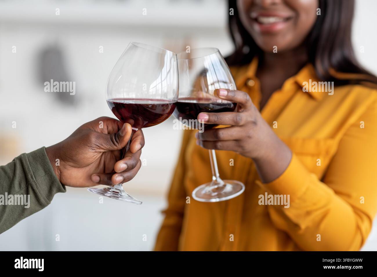 Couple noir heureux trinquant avec des verres de vin rouge dans la cuisine, célébrant la complicité Banque D'Images