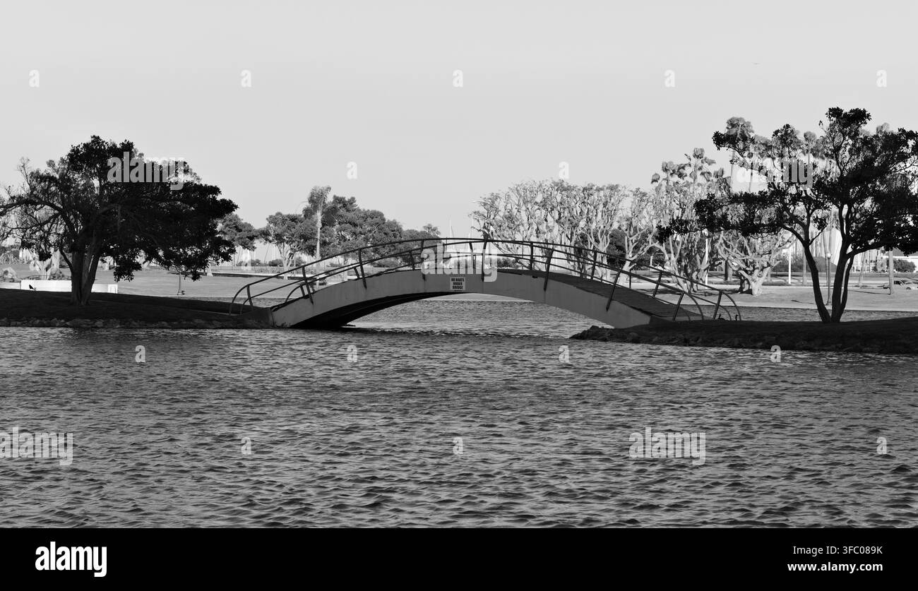 Un pont arqué bleu traverse l'eau ondulante d'un parc riverain de Long Beach. Banque D'Images