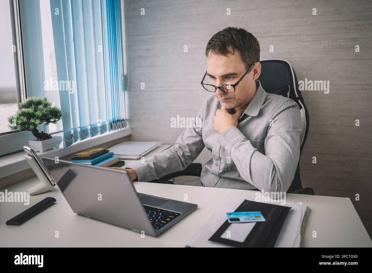 Homme d'affaires pensif caressant sa barbe tout en regardant l'écran de son ordinateur portable. Analyse approfondie, prise de décision et réflexion professionnelle au travail. Banque D'Images
