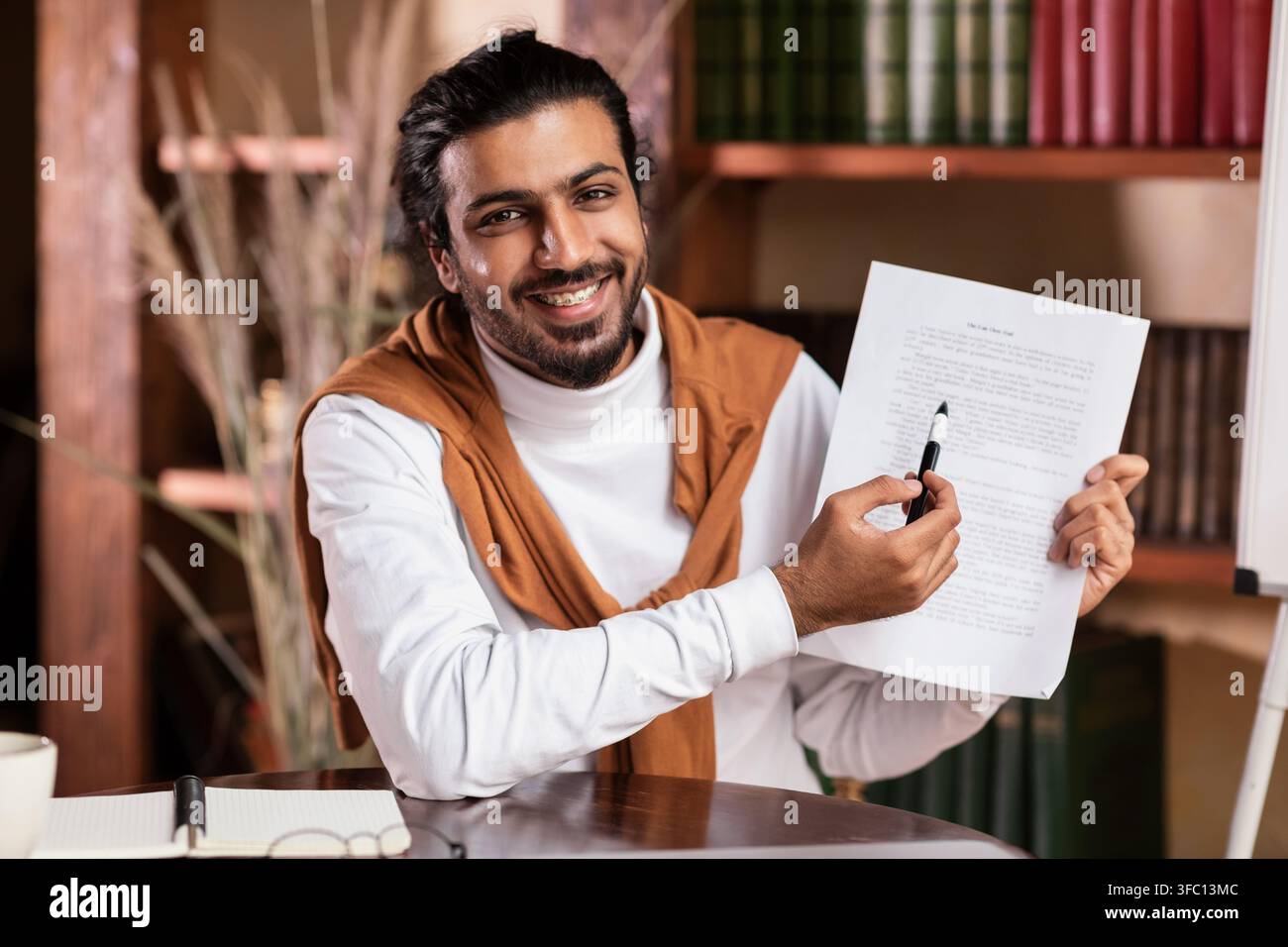 Un bon homme enseignant indien qui montre Essay à l'appareil photo assis à l'intérieur Banque D'Images