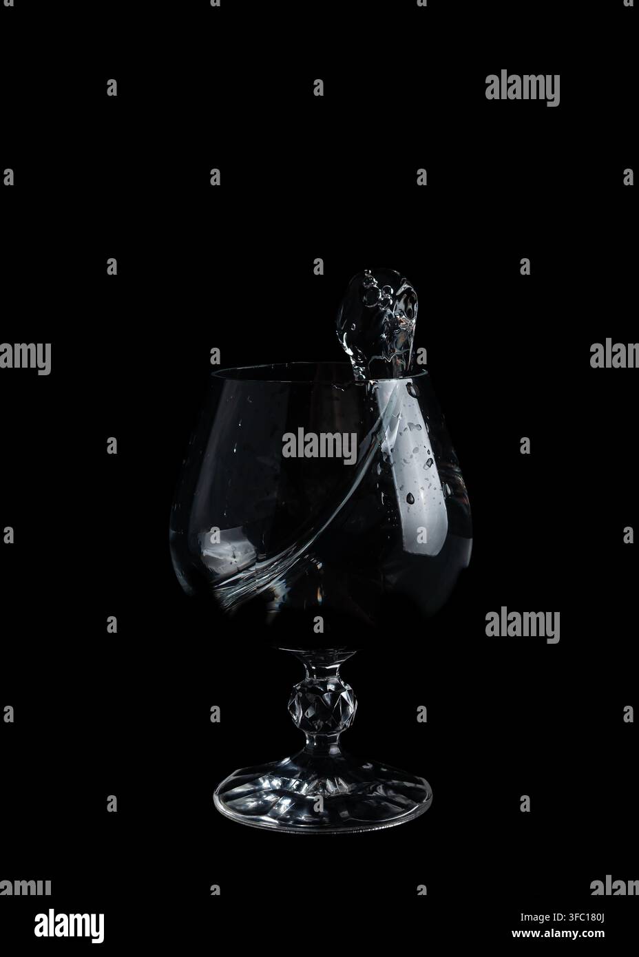 L'eau déborde et crée des éclaboussures dans un verre transparent posé sur une surface noire dans cette scène d'une action simple. Banque D'Images