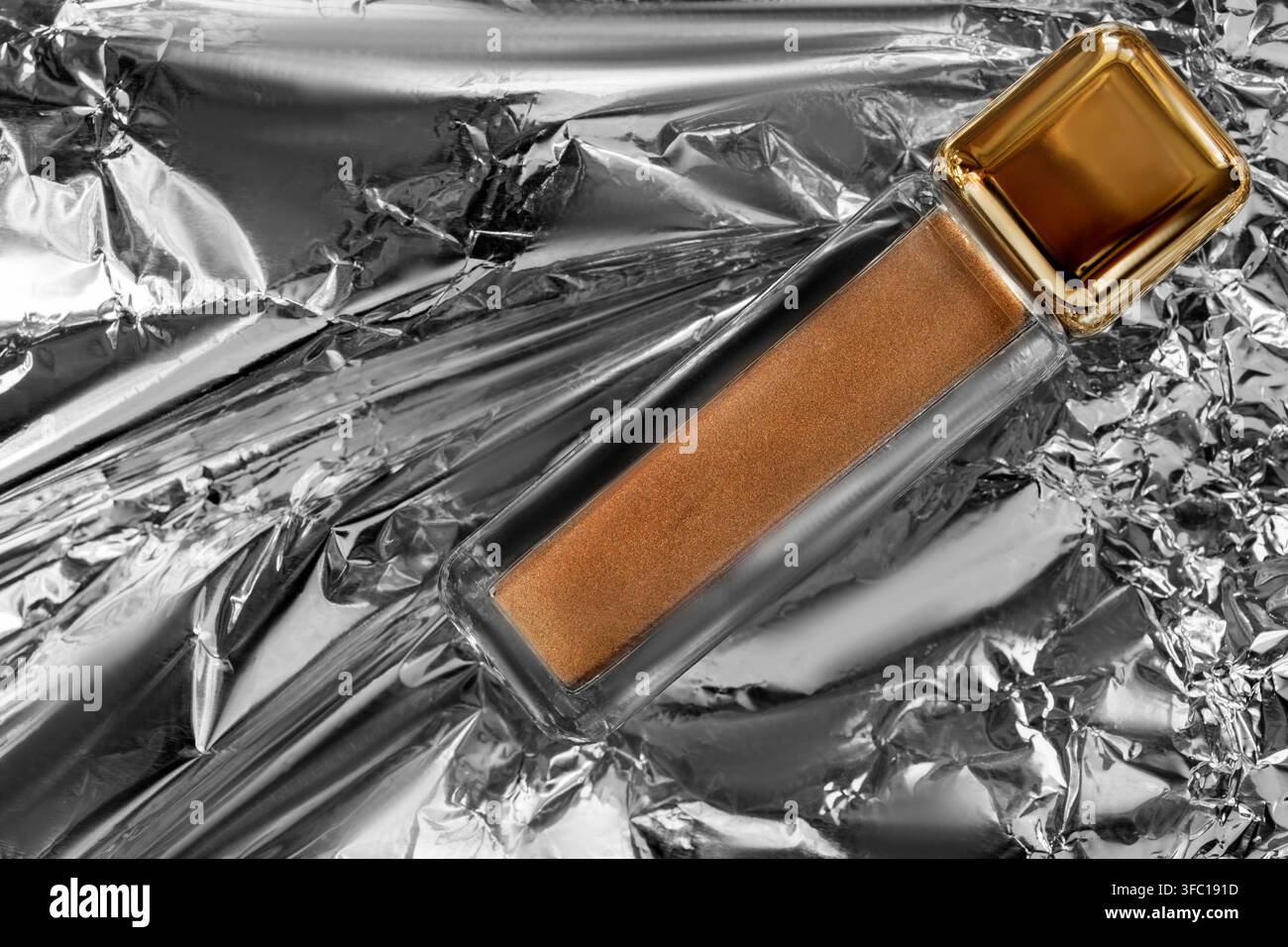 Pot de paillettes de maquillage couleur bronze posé sur un fond de papier d'aluminium froissé Banque D'Images