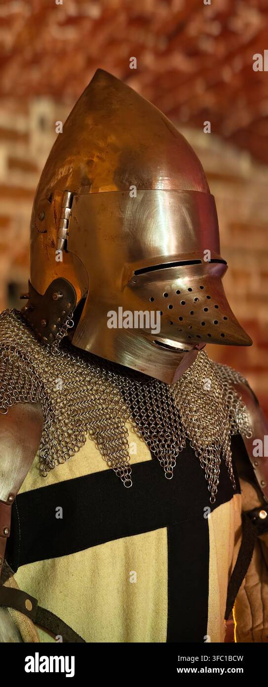 Un plan vertical en gros plan d'un casque de chevalier médiéval détaillé, présentant une visière pointue distinctive et une coiffe en mailles complexes. L'armure est posée Banque D'Images
