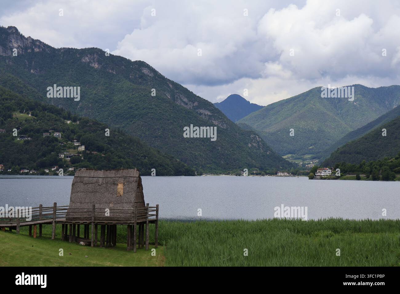 Molina di Ledro, Italie. 6 juin 2026. Reconstruction d'une maison sur pilotis préhistorique au lac de Ledro avec les montagnes du lac de Garde en arrière-plan. Banque D'Images
