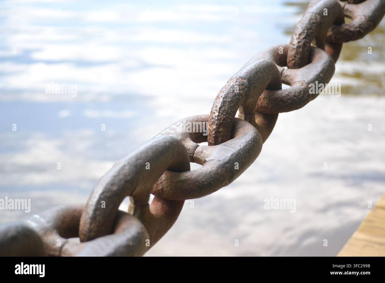 Vue diagonale macro d'une chaîne en fer rouillée et lourde sur une eau floue, avec une faible profondeur de champ et une mise au point sélective sur l'avant-plan. Banque D'Images