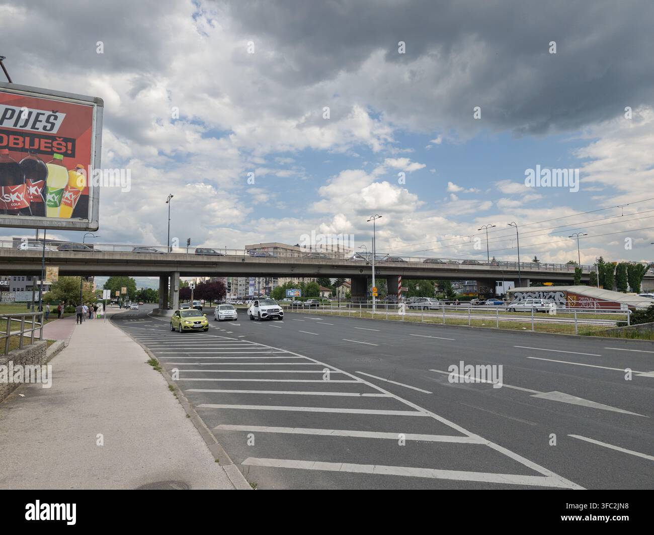 Une vue grand angle d'une route urbaine avec des véhicules passant sous un pont en béton, capturant l'atmosphère d'un trajet quotidien en ville. - Image de stock capturée avec un smartphone