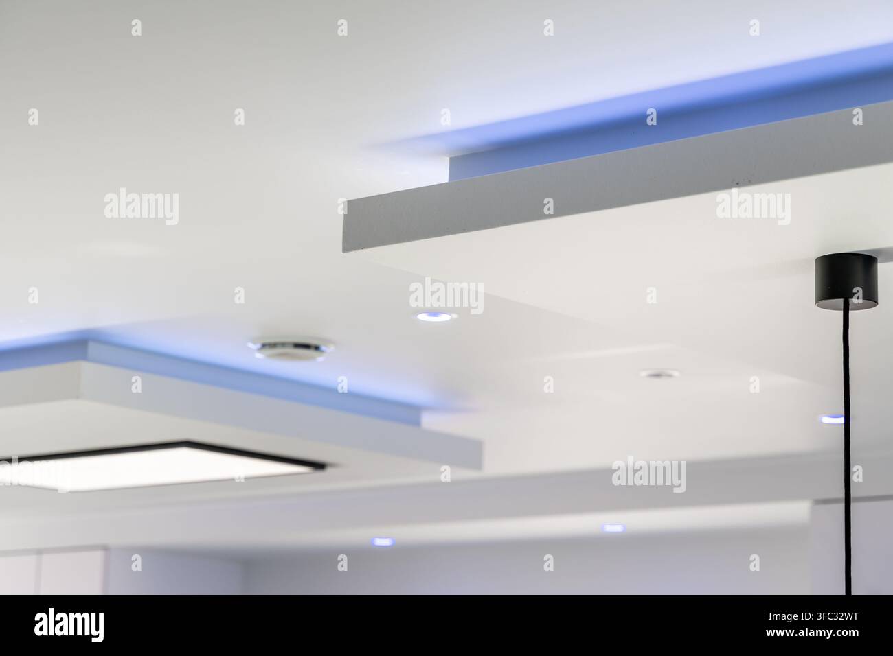Un plafond contemporain présente des éléments architecturaux superposés avec un éclairage intégré et des bandes LED bleues subtiles créant une atmosphère sophistiquée Banque D'Images