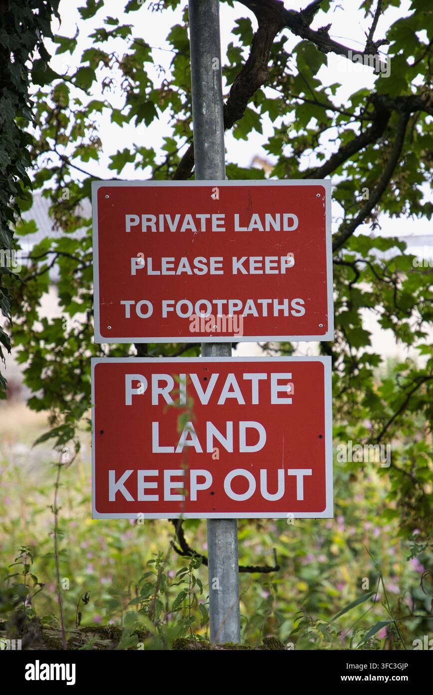 Panneaux d'avertissement rouges empilés sur un poteau métallique indiquant Terrain Privé Veuillez Rester sur les Sentiers et Terrain Privé Défense d'Entrée. Banque D'Images