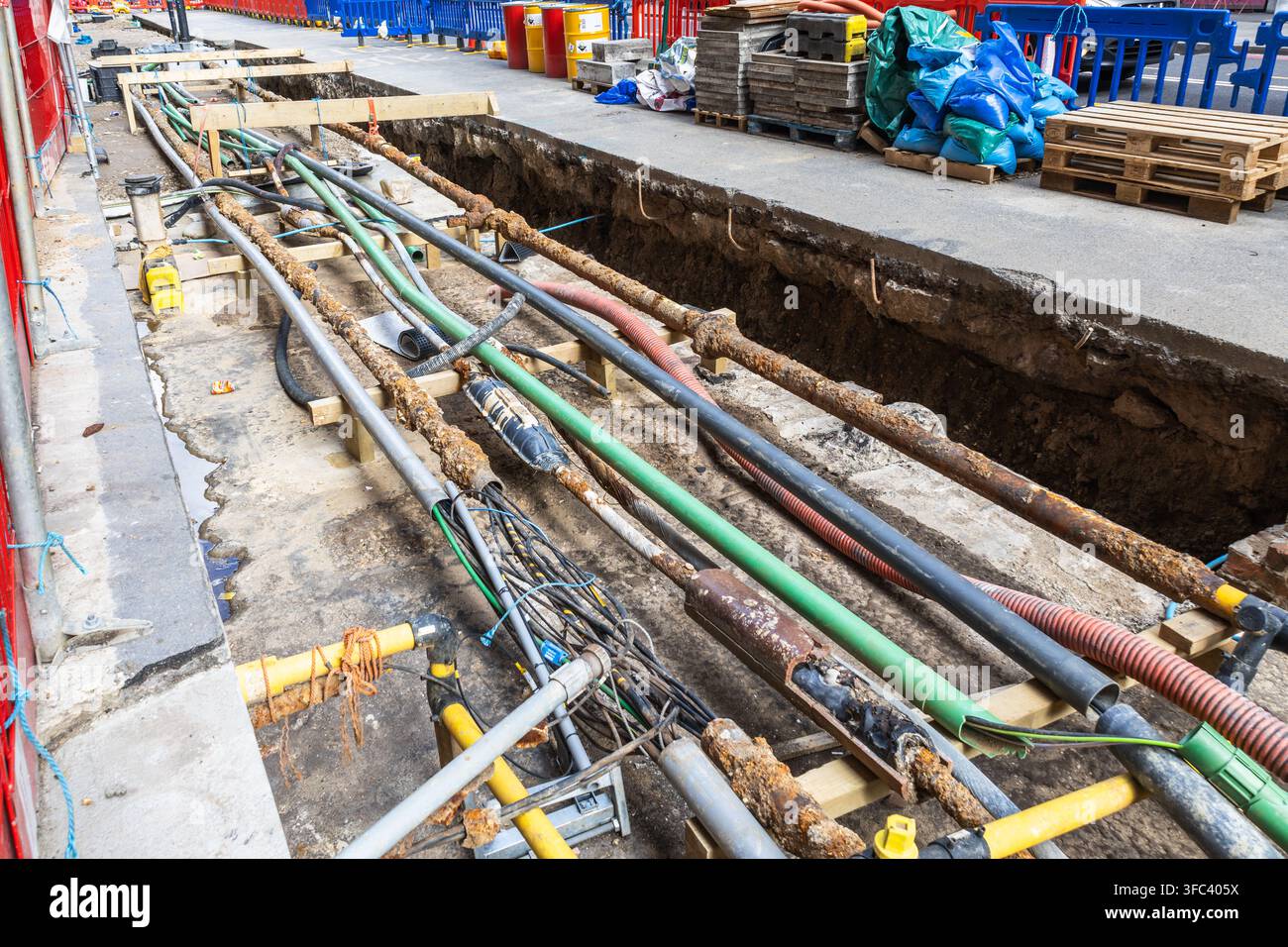Lignes et tuyaux utilitaires exposés dans une tranchée de construction routière Banque D'Images