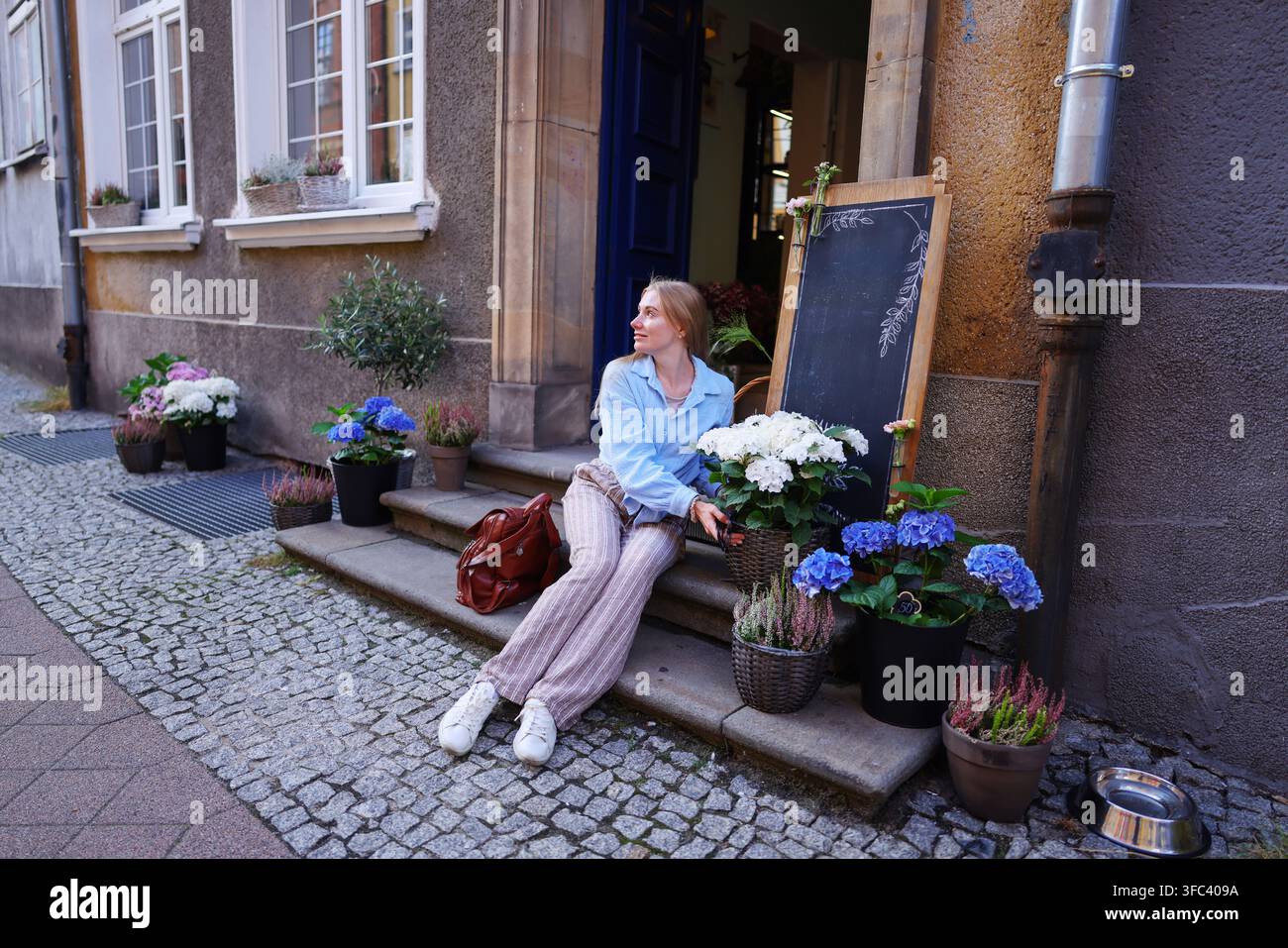 Touriste élégante assise près d'une boutique de fleurs avec des hortensias bleus et blancs dans un charmant quartier européen. Banque D'Images