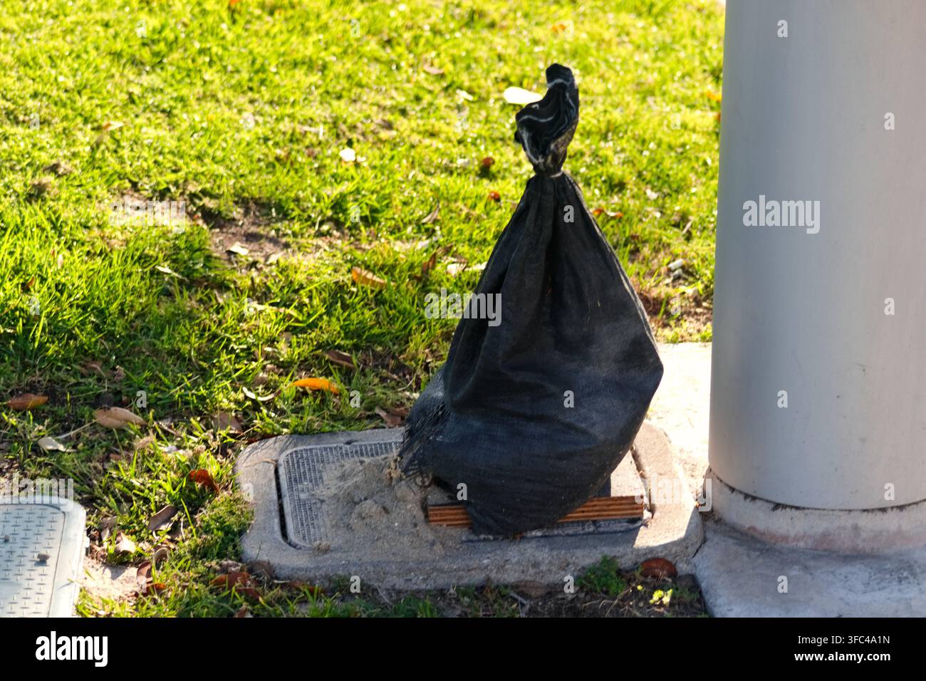 Un sac de sable noir se trouve près d'une colonne et d'un couvercle d'utilité dans un parc de Long Beach Banque D'Images