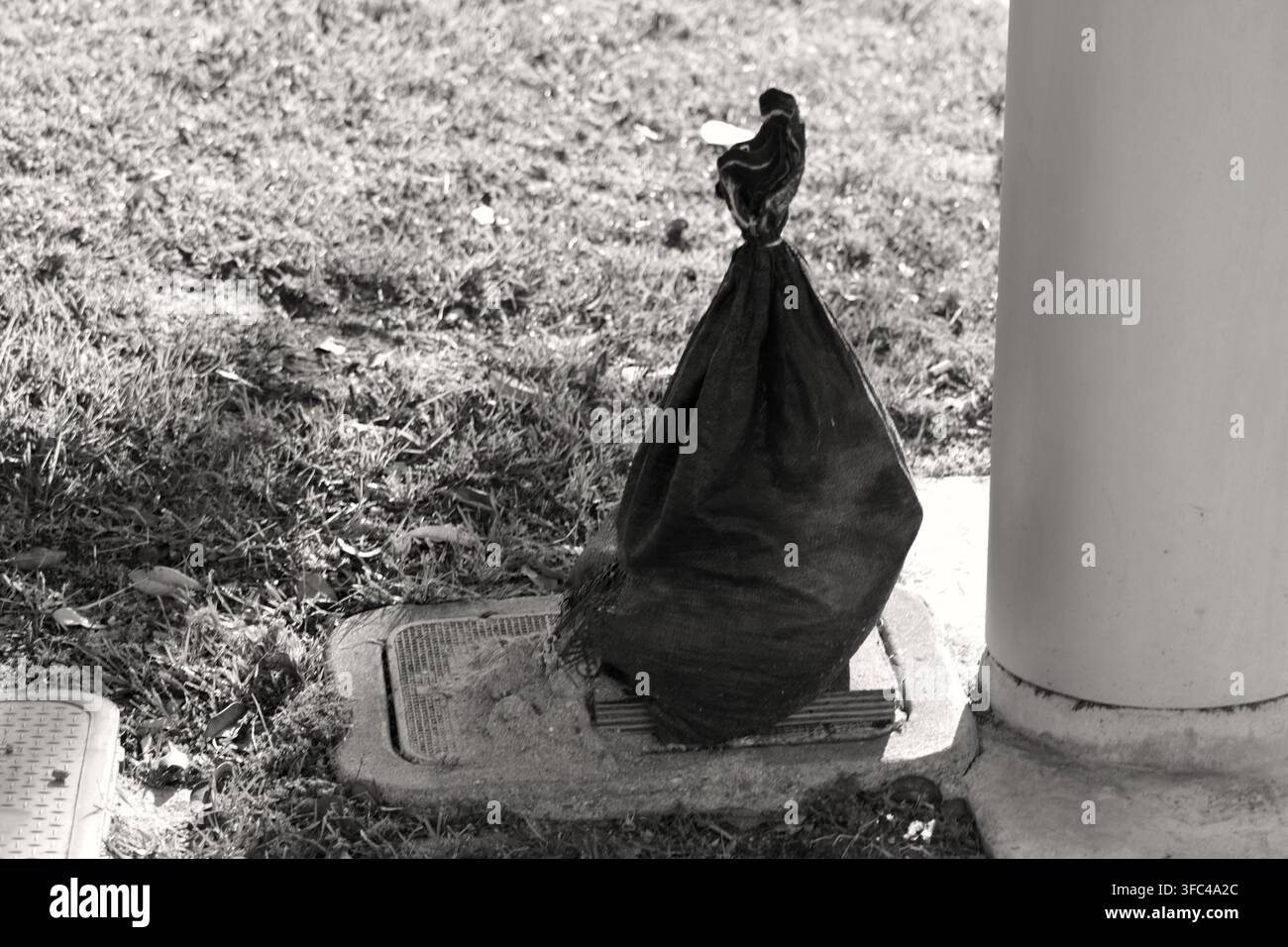 Un sac de sable noir se trouve près d'une colonne et d'un couvercle d'utilité dans un parc de Long Beach Banque D'Images