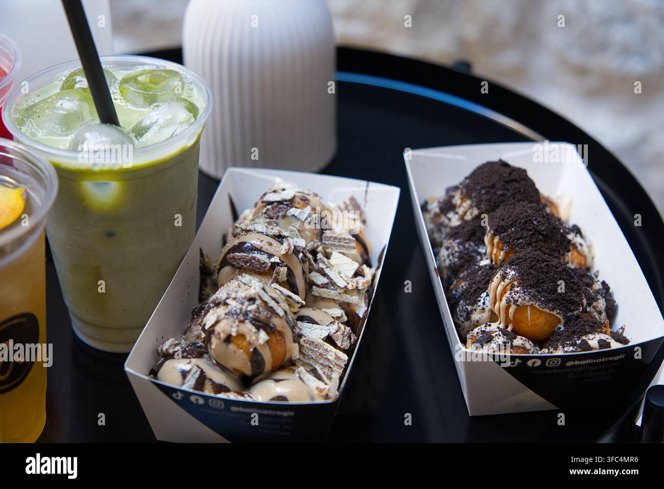 Plateaux de boules de pâte à dessert sucrées garnies de sauce au chocolat, de gaufrettes concassées et de miettes de biscuits, servies accompagnées de boissons glacées au matcha latte Banque D'Images