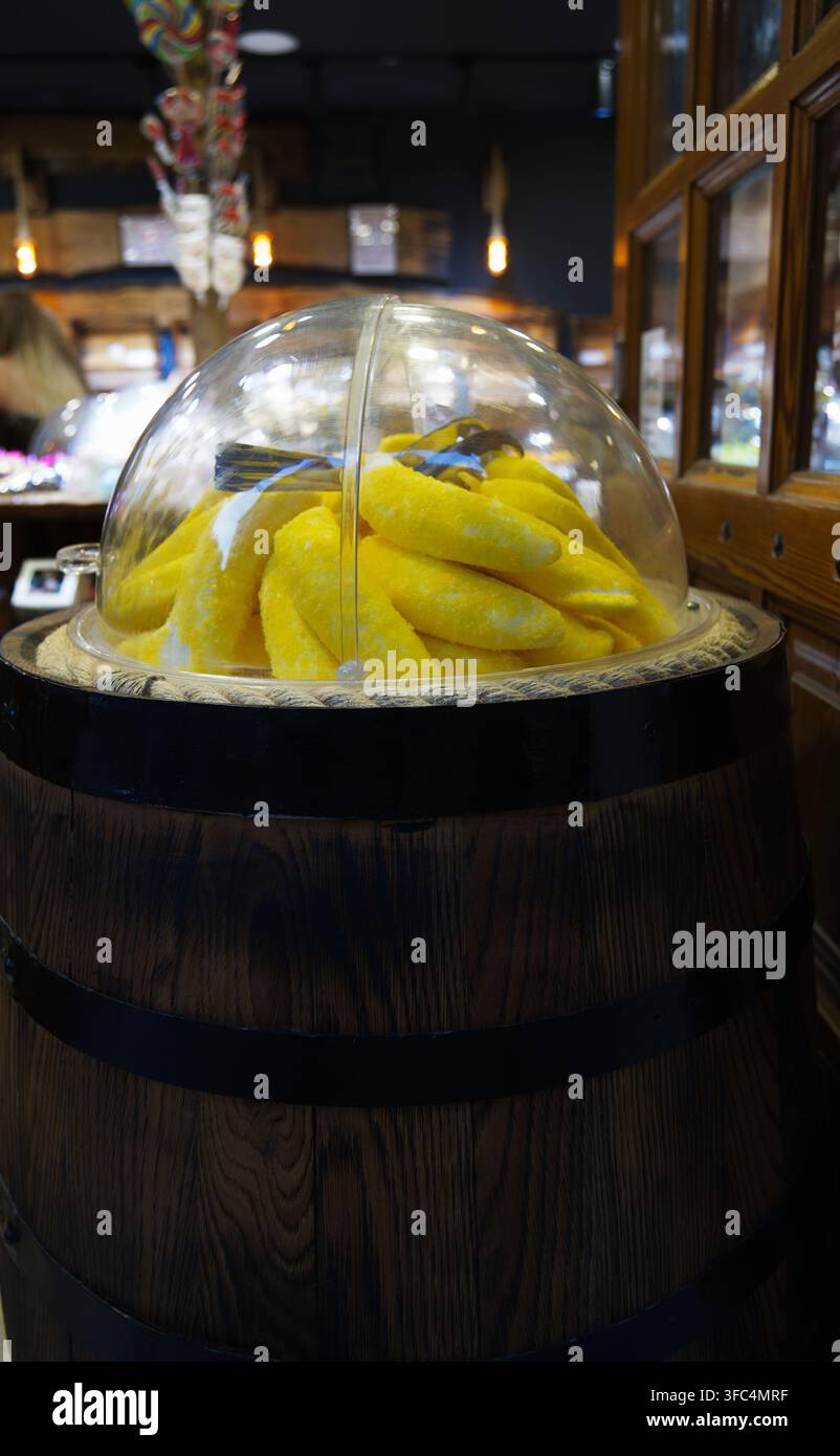 Bonbons gélatineux en forme de banane jaunes exposés sous un dôme en plastique transparent posé sur un tonneau en bois vintage Banque D'Images