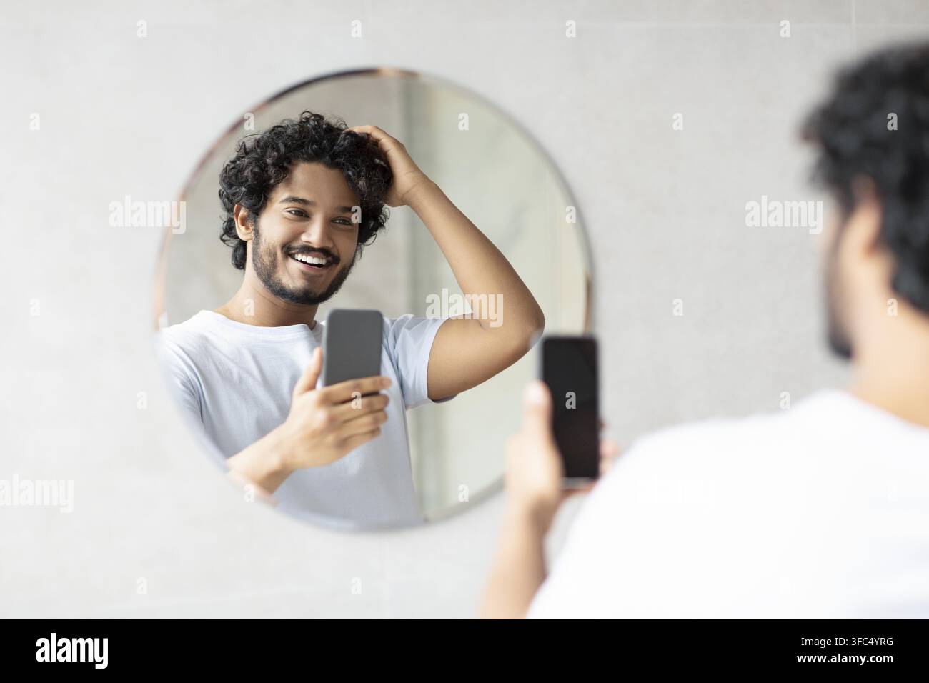 Jeune homme sud-asiatique souriant prenant un selfie devant le miroir, cadre de salle de bain Banque D'Images