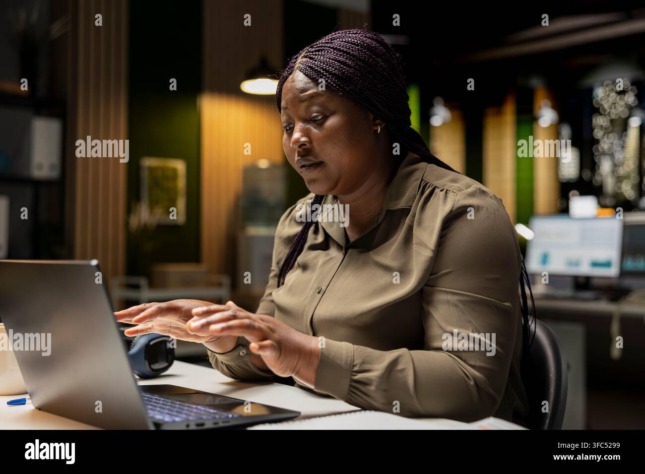 Une femme d'affaires noire participe à un appel vidéo à distance depuis son bureau sombre, maintenant un contact visuel avec la webcam. Participation à une réunion pour une conversation significative, établissant des relations et des connexions. Banque D'Images