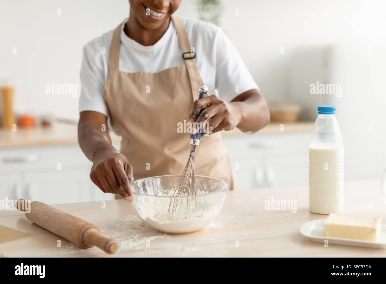 Boulangère noire souriante fouettant un mélange de farine dans une cuisine moderne, concept de cuisine maison Banque D'Images