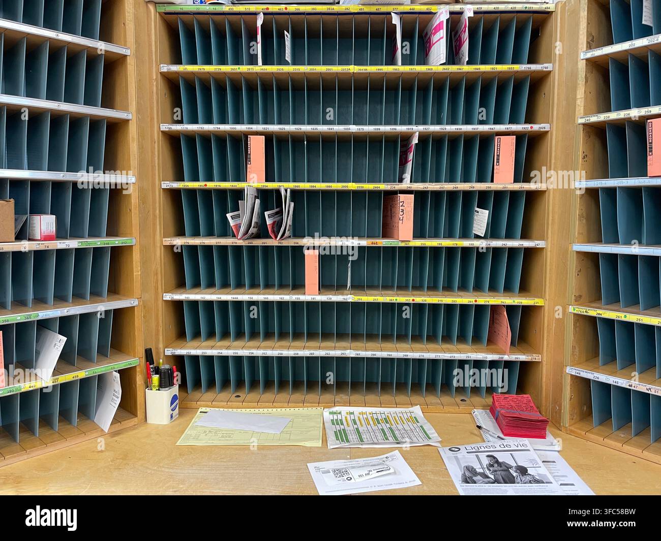 Intérieur d'un bureau de poste canadien avec un grand casier de tri postal en bois, des casiers bleus numérotés contenant des lettres et des colis, des papiers de tri sur le bureau - Image de stock capturée avec un smartphone