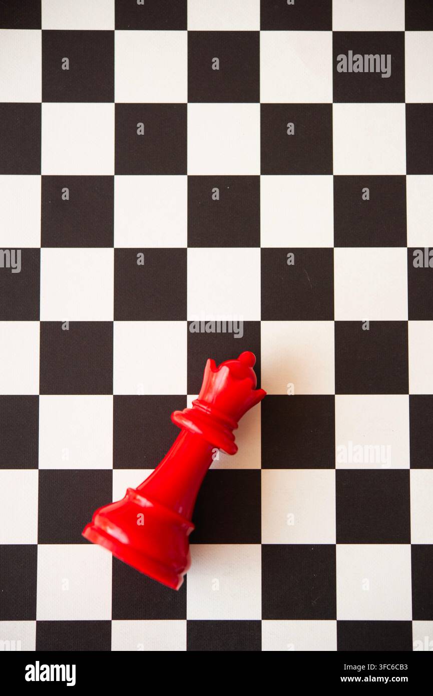 Pièce d'échecs Dame rouge couchée sur un échiquier noir et blanc, symbolisant la défaite, la perte, la stratégie et un coup raté Banque D'Images