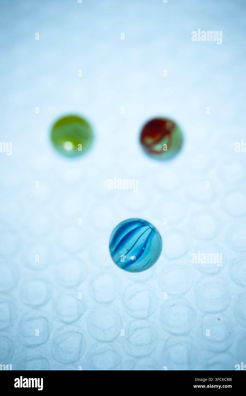 Marbre de verre lue en mise au point nette avec des billes vertes et rouges floues en arrière-plan sur une surface texturée bleu pâle, créant une nature morte abstraite ludique Banque D'Images