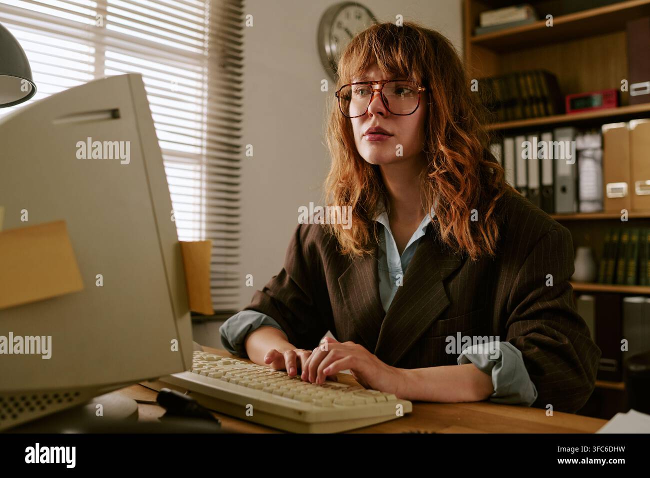 Femme concentrée tapant sur un ordinateur rétro dans un bureau vintage Banque D'Images