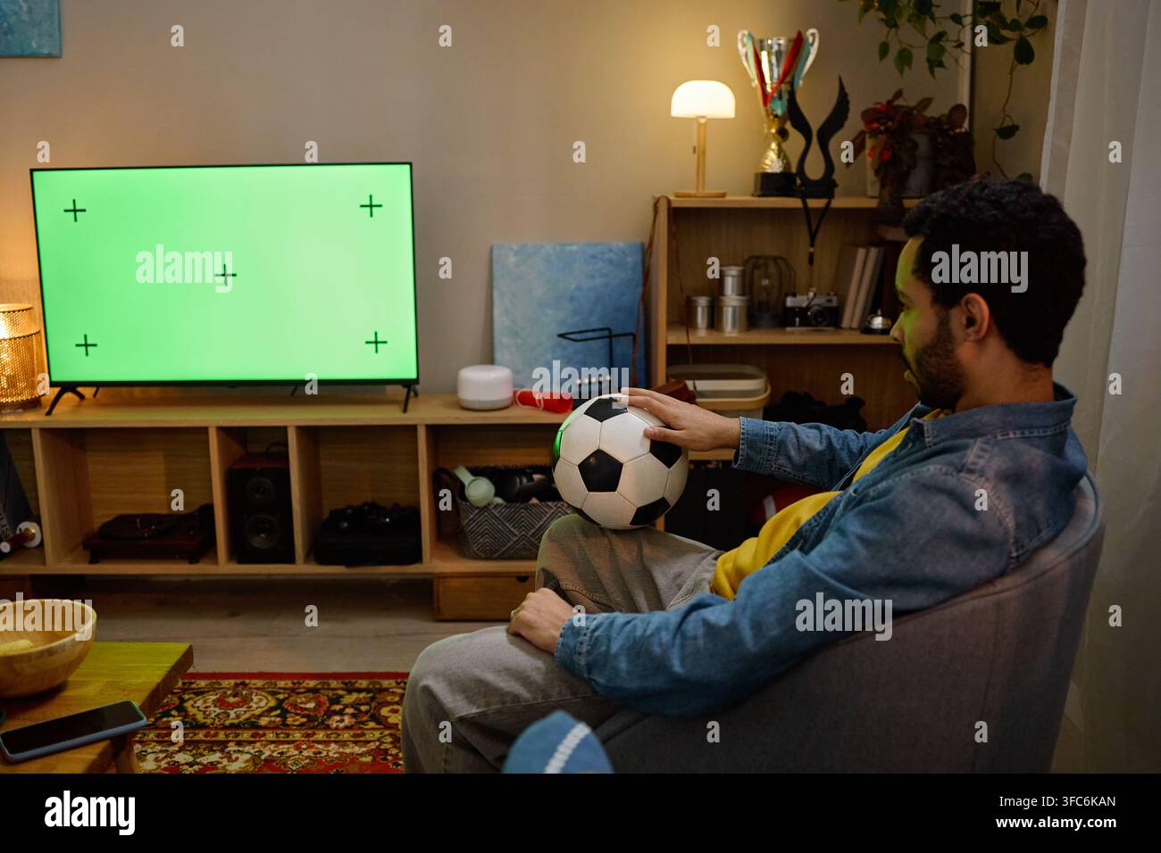 Homme tenant un ballon de football regardant une télévision à écran vert Banque D'Images