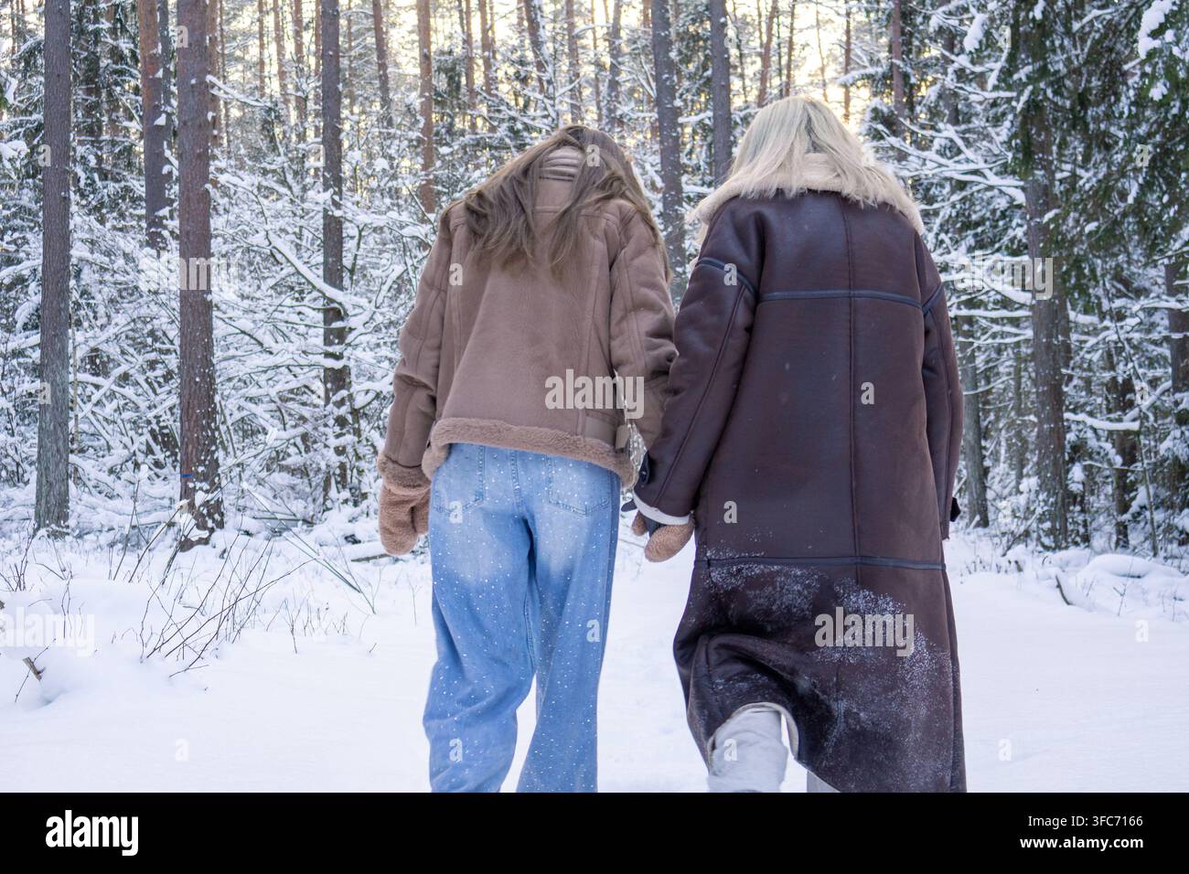 Mère et fille marchent ensemble à travers une forêt enneigée, vues de dos lors d'une sortie hivernale. Concept de lien familial et de voyage partagé à travers p Banque D'Images