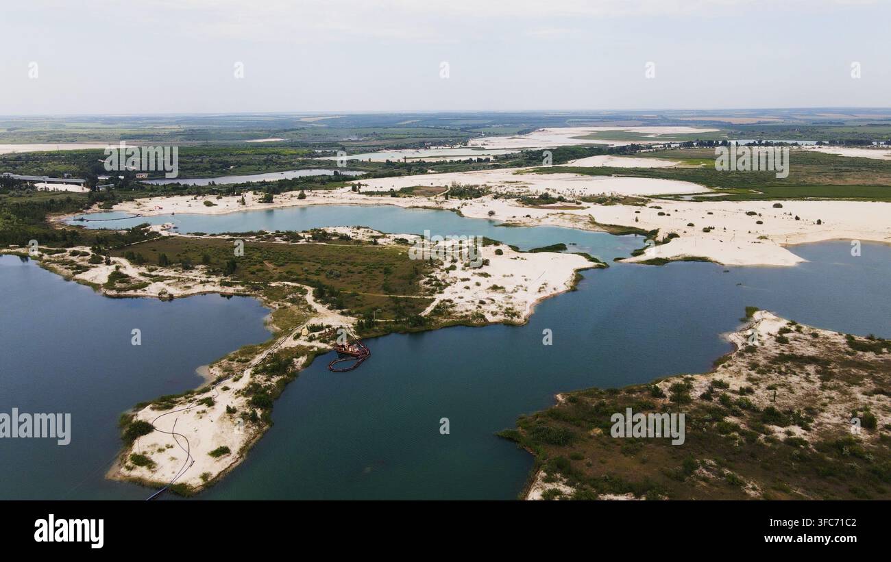 Vue aérienne de l'extraction industrielle du sable créant des lacs artificiels avec une eau turquoise peu profonde et une eau bleu foncé Banque D'Images