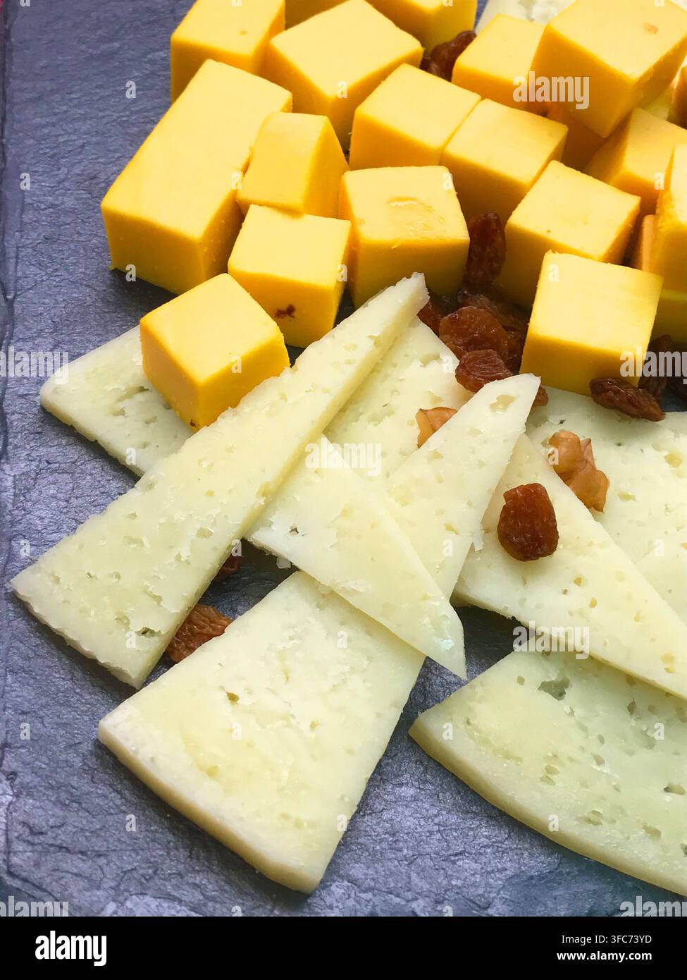 Fromages variés avec raisins secs sur une assiette en ardoise. Banque D'Images