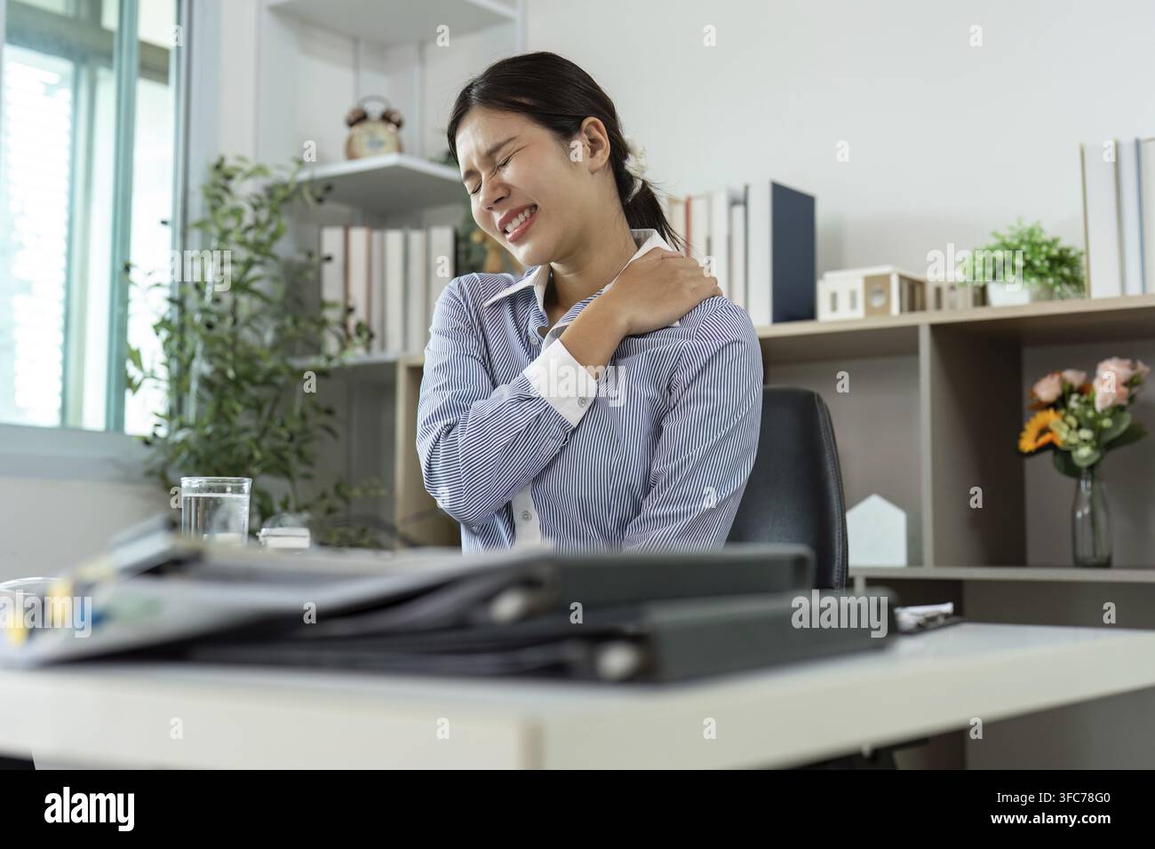 Une femme grimace de douleur tout en gardant son épaule sur son bureau et met en évidence les effets du syndrome du bureau Banque D'Images