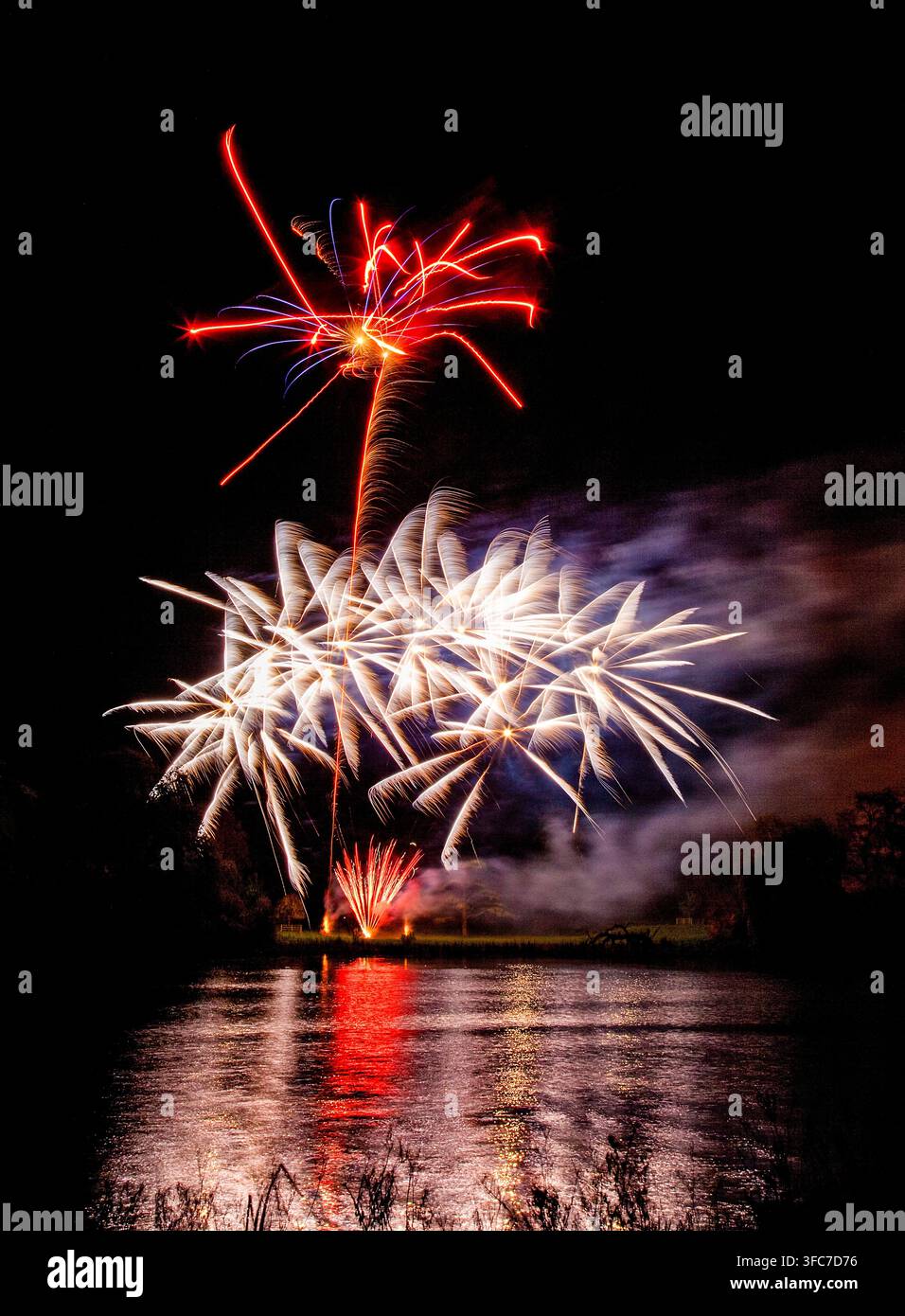 Affichage de feux d'artifice colorés et vifs éclatant au-dessus d'un lac avec des reflets dramatiques rouges et blancs dans l'eau Banque D'Images