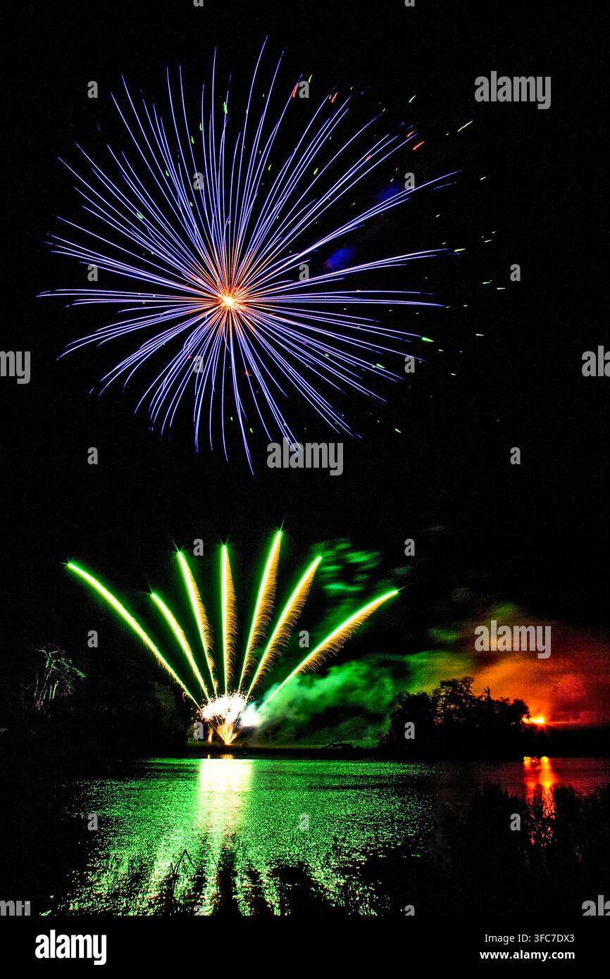 Spectacle de feux d'artifice éclatants et colorés éclatant au-dessus d'un lac avec des reflets dramatiques verts et orange dans l'eau Banque D'Images