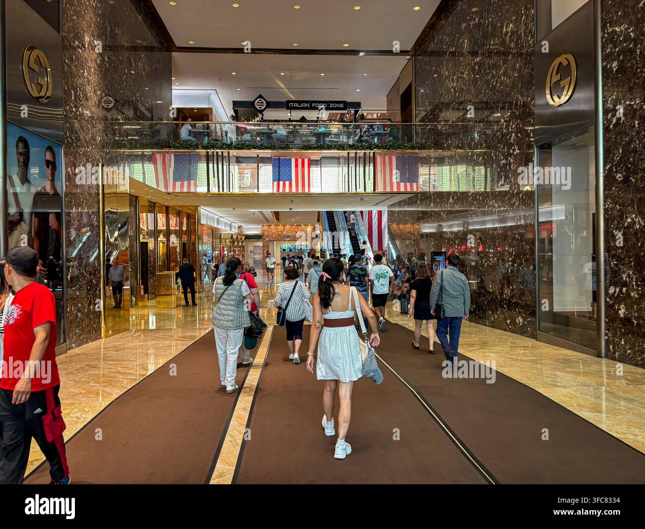 Les visiteurs traversent l'atrium en marbre du Trump Tower, passant devant le magasin Gucci et des rangées de drapeaux américains. New York, New York, États-Unis, 7 août 2 Banque D'Images