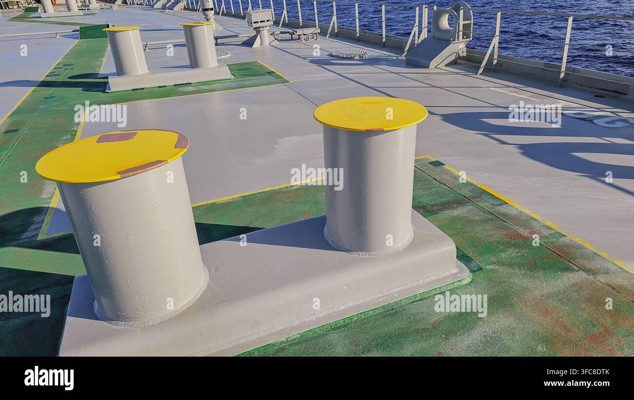 Vue rapprochée d'un bitt double en acier jaune servant d'amarrage sur le pont du navire avec de l'eau de mer bleue en arrière-plan par une journée calme et ensoleillée, photo horizontale en stock. Banque D'Images