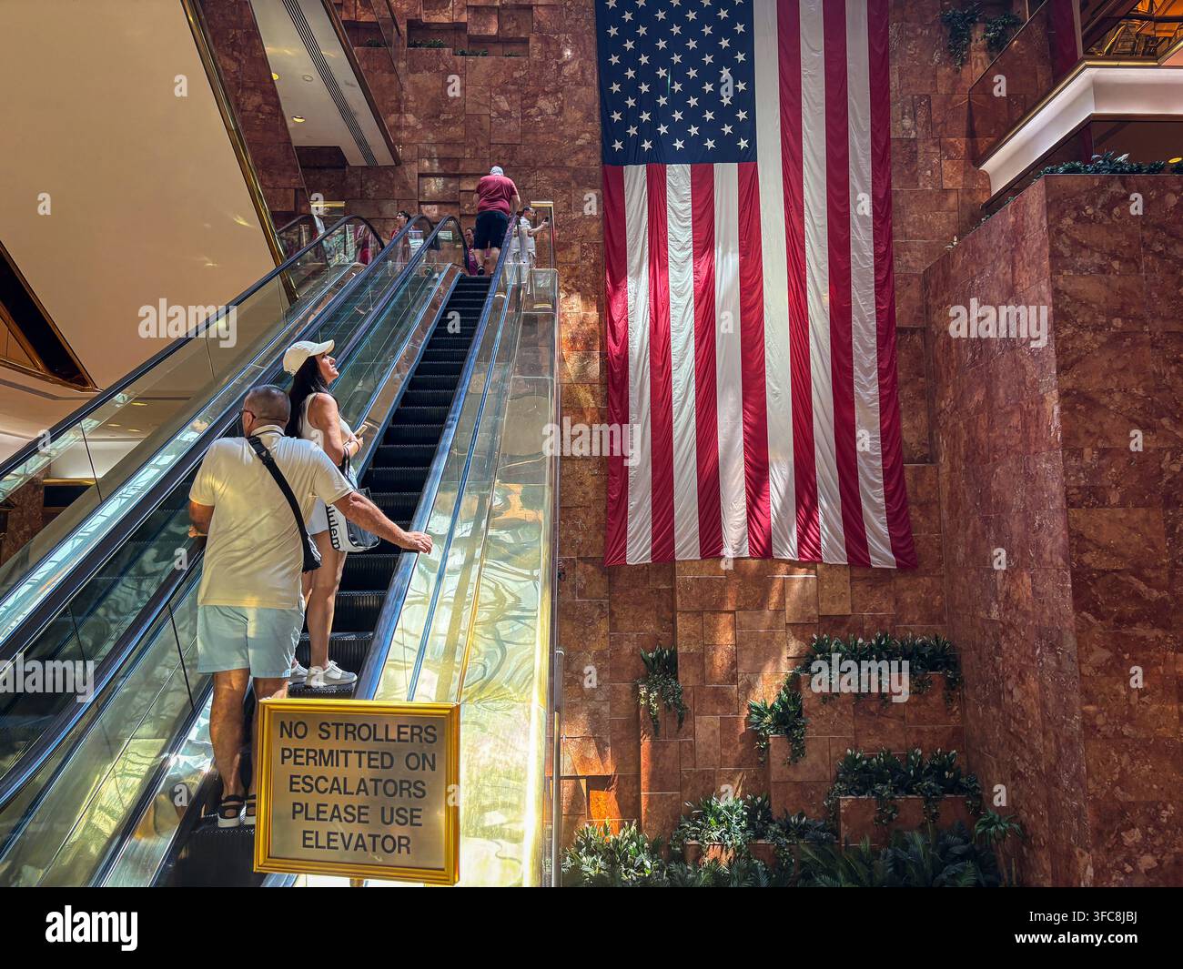 Les visiteurs empruntent les escalators de l'atrium du Trump Tower à côté d'un drapeau américain accroché au mur de marbre rose. New York, New York, États-Unis, 7 Augu Banque D'Images