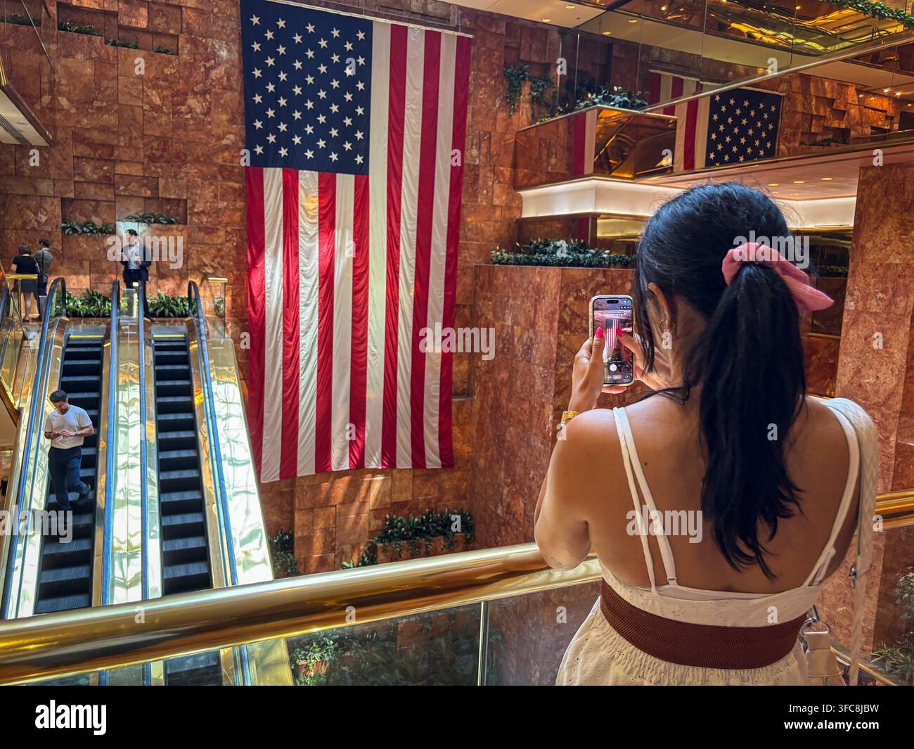 Un visiteur photographie avec son téléphone un drapeau américain accroché dans l'atrium du Trump Tower. New York, New York, États-Unis, 7 août 2026. Banque D'Images