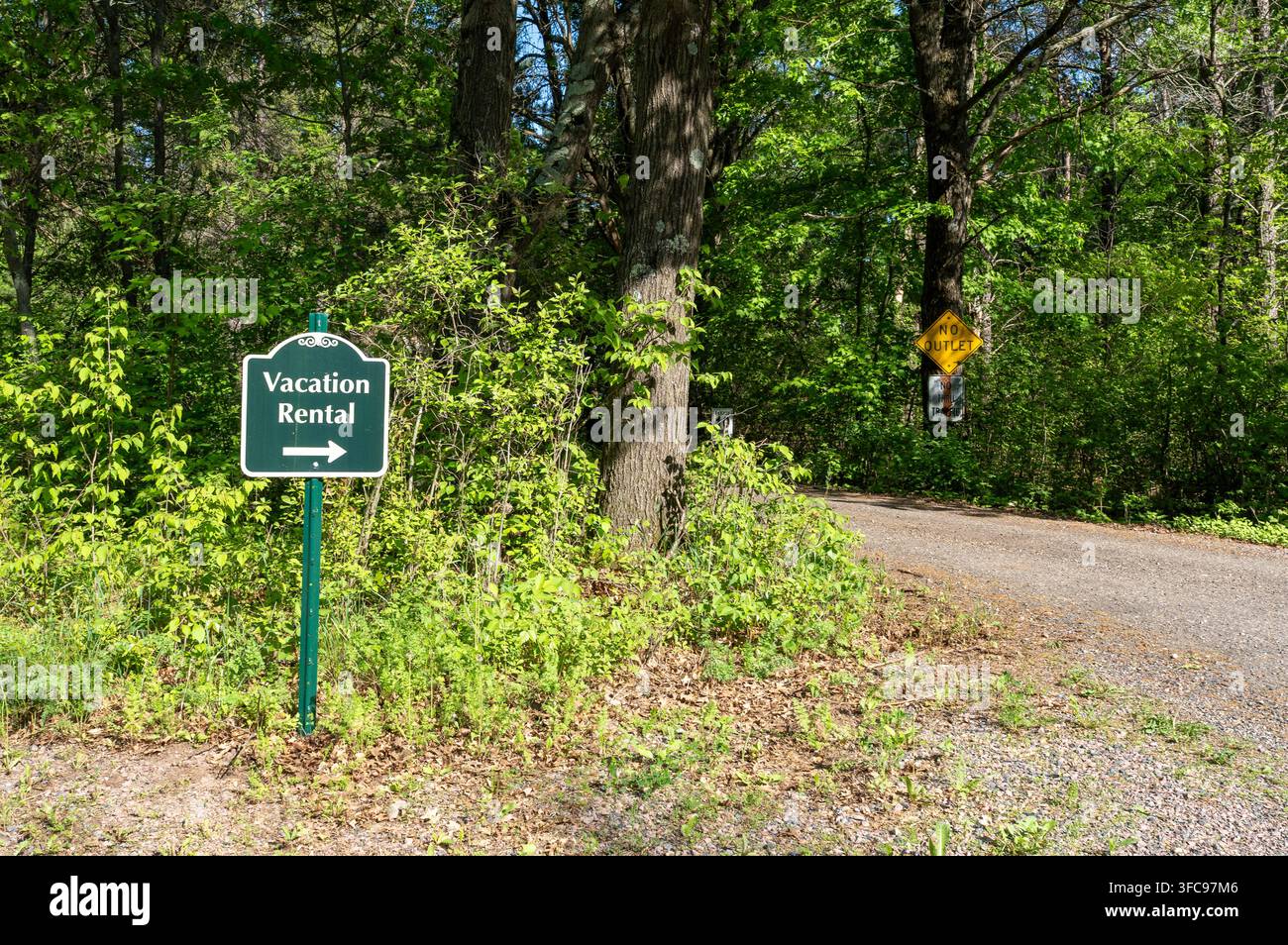 Panneau vert indiquant une "Location de vacances" à côté d'une route de gravier dans une zone rurale boisée. Des panneaux supplémentaires indiquant "Pas de sortie" et "Pas de circulation de transit" sont visibles Banque D'Images