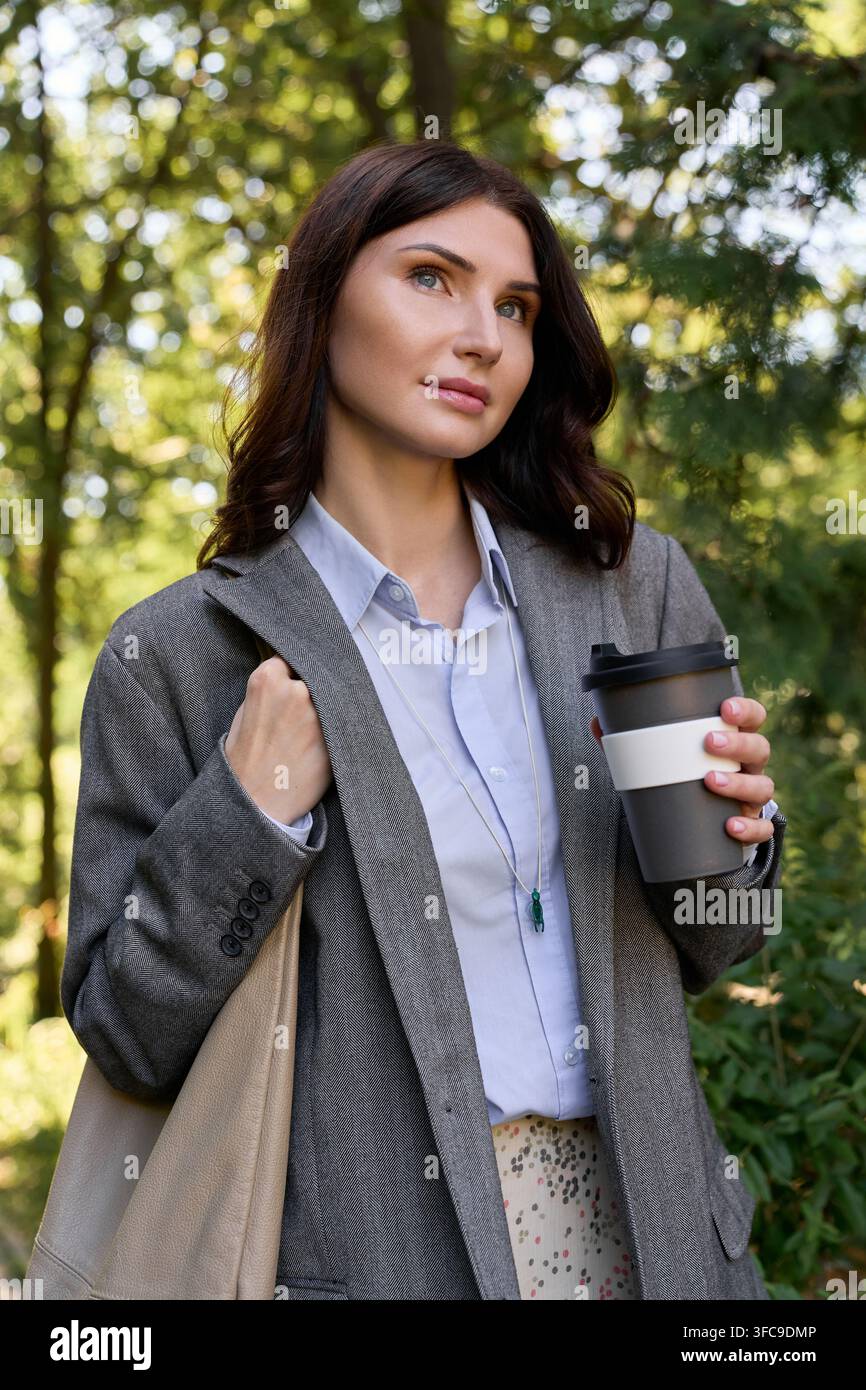 Femme en blazer gris profitant de l'air frais dans un parc paisible, se déconnectant des écrans Banque D'Images