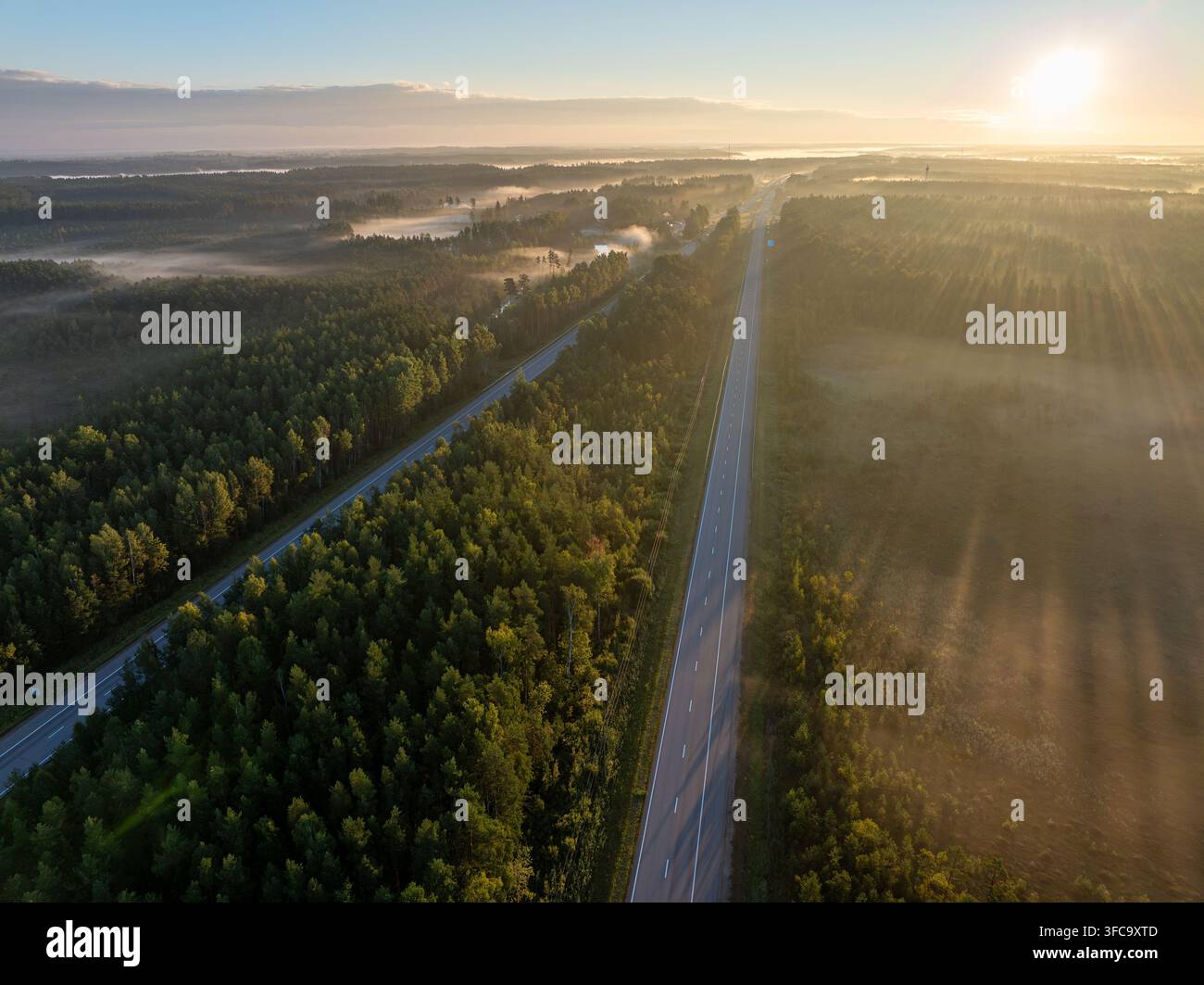 Vue aérienne de l'autoroute A2 E77 traversant une forêt et un paysage brumeux près de Sigulda, Lettonie, au lever du soleil Banque D'Images