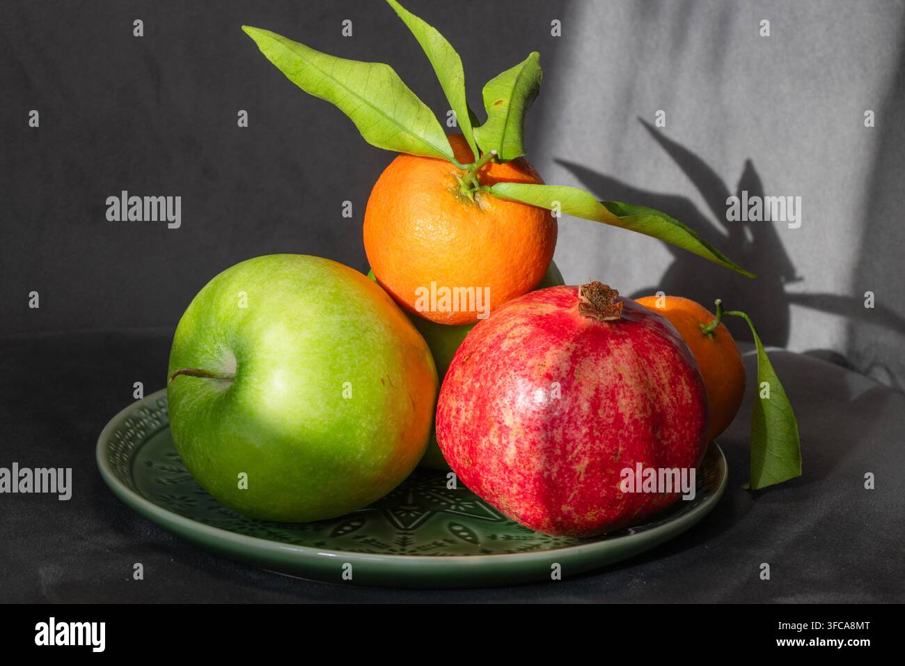 Un arrangement coloré de fruits citriques frais et d'une grenade rouge mûre avec des feuilles vertes repose ensemble sur une assiette. Banque D'Images
