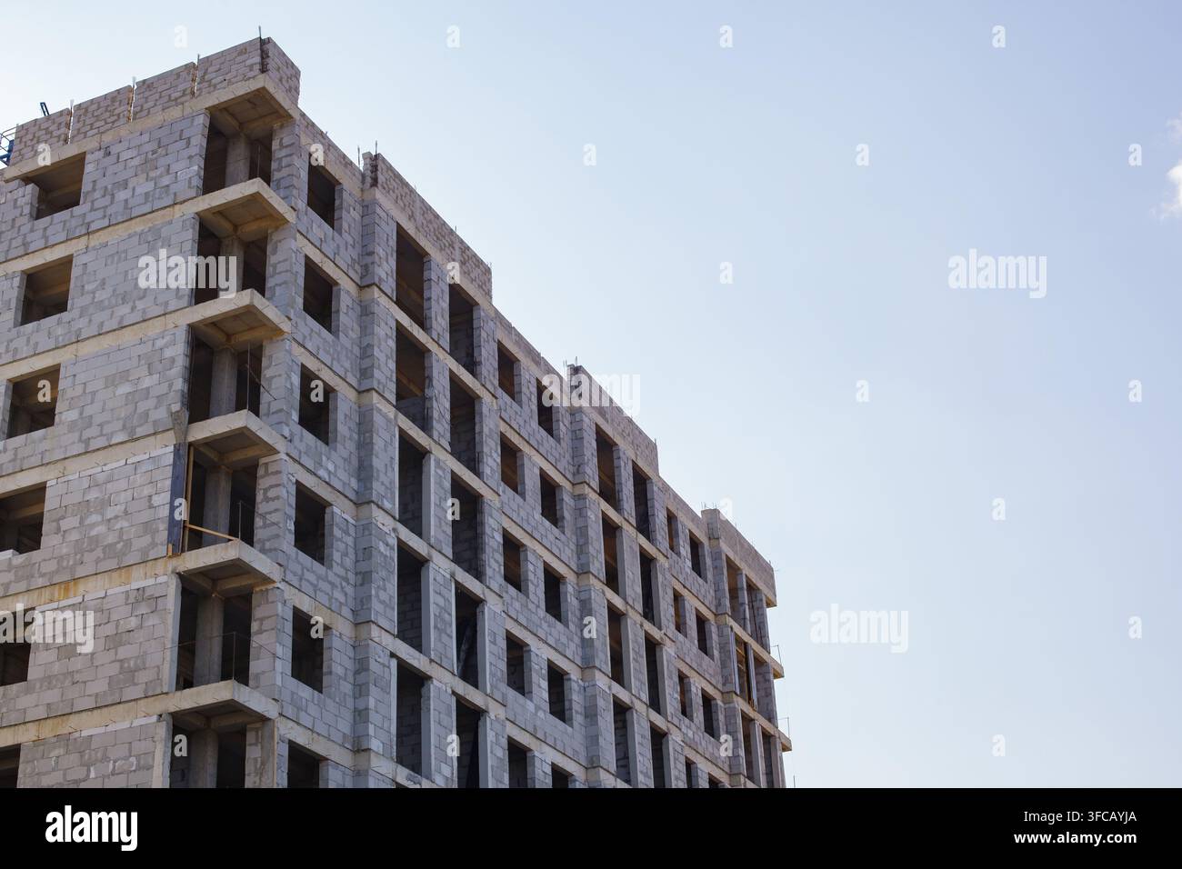Vue en contre-plongé d'un bâtiment résidentiel à plusieurs étages en cours de construction, fait de blocs de béton, contre un ciel bleu clair, offrant un espace de copie généreux pour ur Banque D'Images