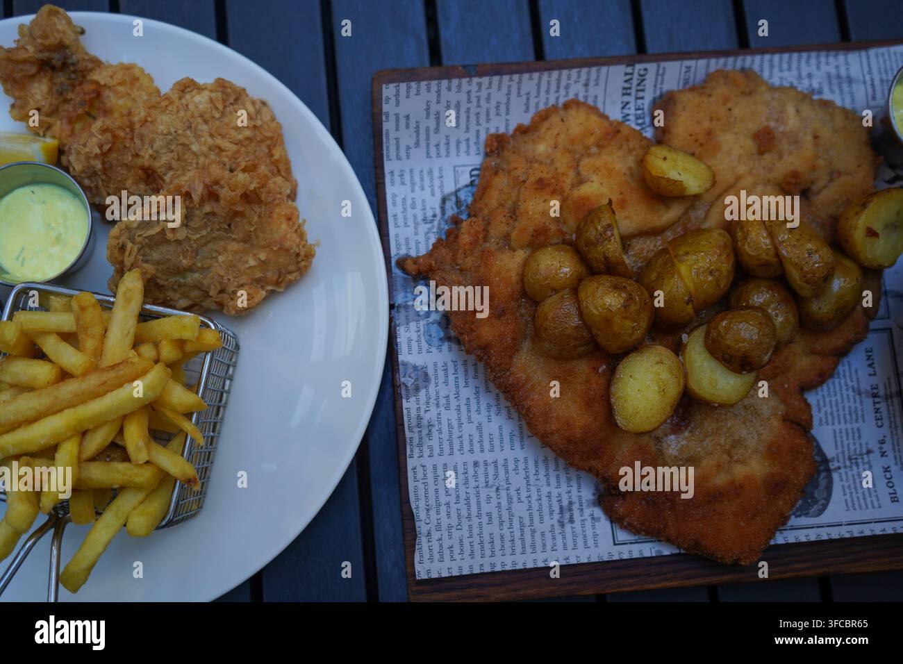 Repas polonais traditionnel avec un énorme escalope de porc panée surmontée de petites pommes de terre rôties accompagnées de poisson frit croustillant et de frites. Banque D'Images
