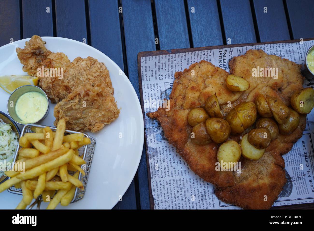 Repas polonais traditionnel avec un énorme escalope de porc panée surmontée de petites pommes de terre rôties accompagnées de poisson frit croustillant et de frites. Banque D'Images