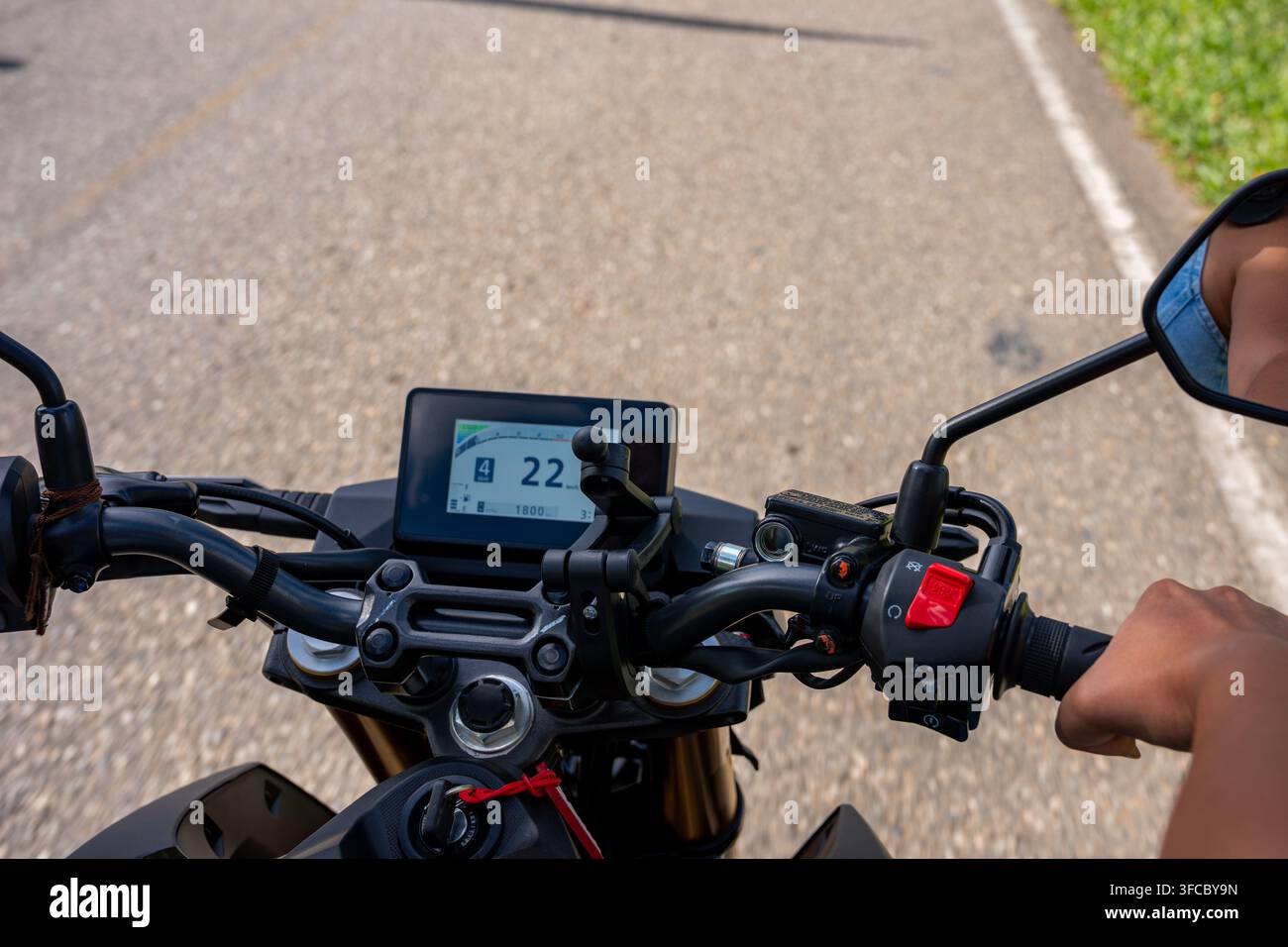 Une personne conduit une moto, montrant une perspective à la première personne du guidon, du tableau de bord numérique et de la route ouverte qui s'étend devant elle, incarnant Banque D'Images