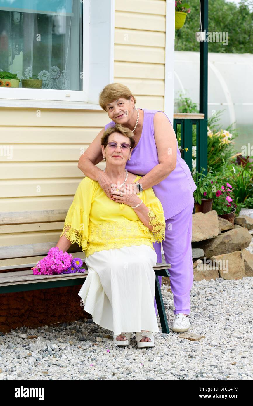 Portrait authentique de deux sœurs russes âgées de 80 et 75 ans assises sur un banc près d’un porche de maison dans un jardin d’été en Russie Banque D'Images