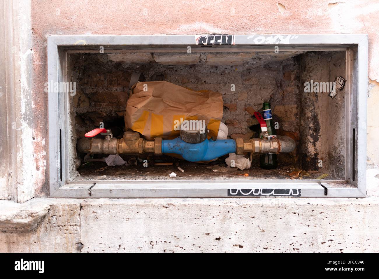 Boîte de compteur d'eau publique intégrée à un vieux mur, taguée de graffitis locaux, jonchée d'emballages en plastique et d'une bouteille en verre vide, Rome, Italie Banque D'Images