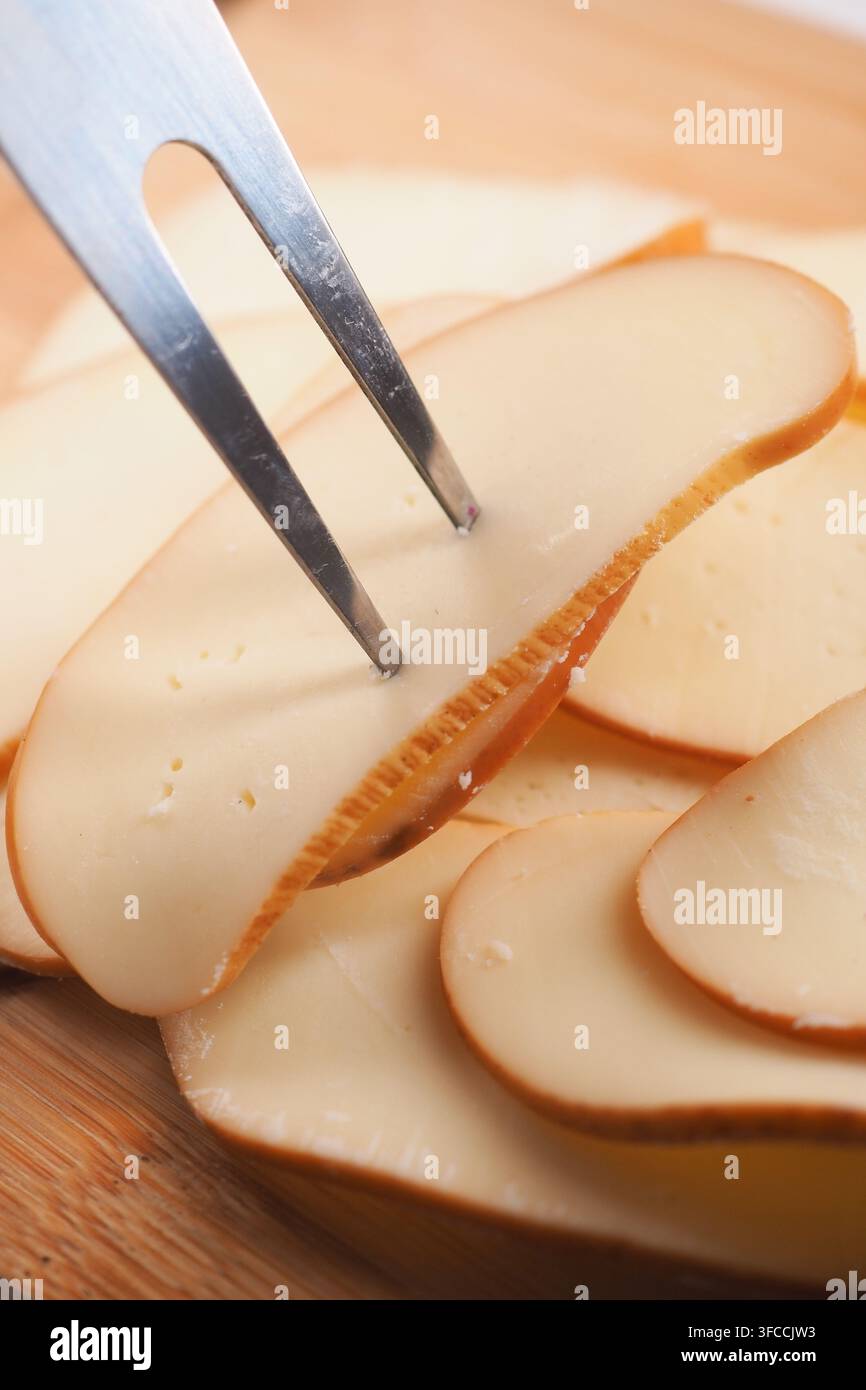 des tranches minces de fromage fumé, comme du Gouda fumé, sur une planche à découper en bois Banque D'Images