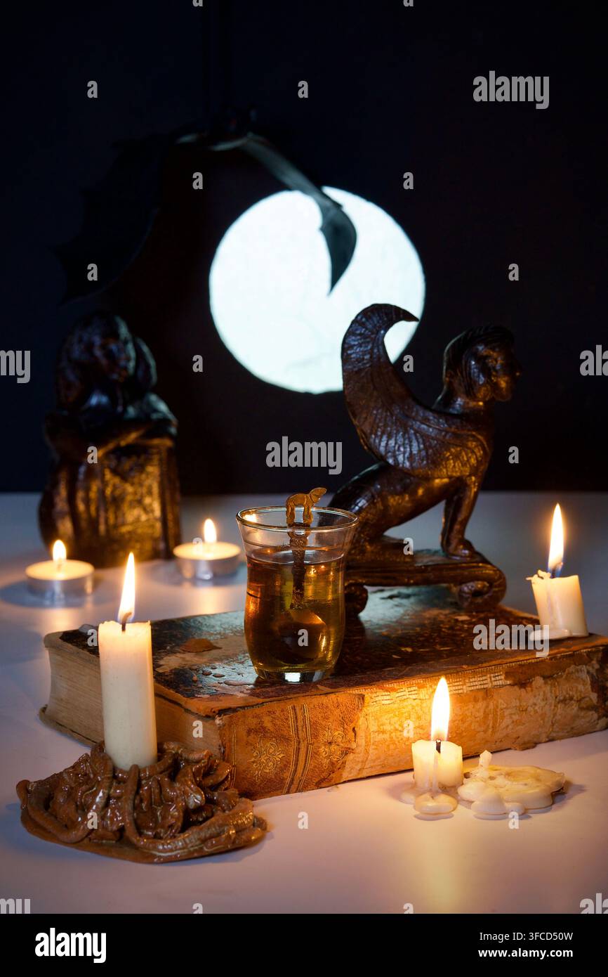 Deux verres de thé dans un décor égyptien avec des statues et des bougies. Un vieux livre et la pleine lune. Les ailes d'une chauve-souris en arrière-plan. Banque D'Images